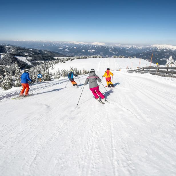 Eine Gruppe von Skifahrern fährt auf einer schneebedeckten Piste bergab.