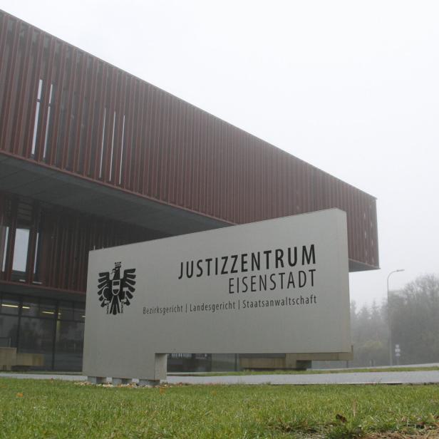 Modernes Justizzentrum mit großem Schild und Rasenfläche im Vordergrund, dahinter nebliges Wetter und Bäume.