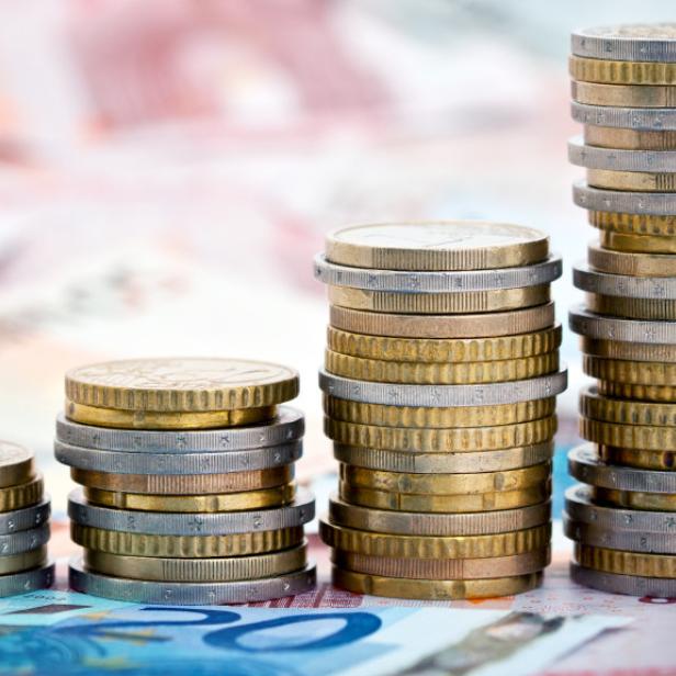 Auf Geldscheinen gestapelte Euro-Münzen in vier unterschiedlich hohen Stapeln.