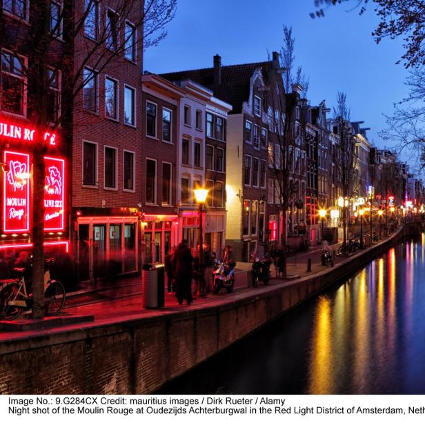 Nachts im Rotlichtviertel von Amsterdam mit dem Moulin Rouge und einem Kanal.