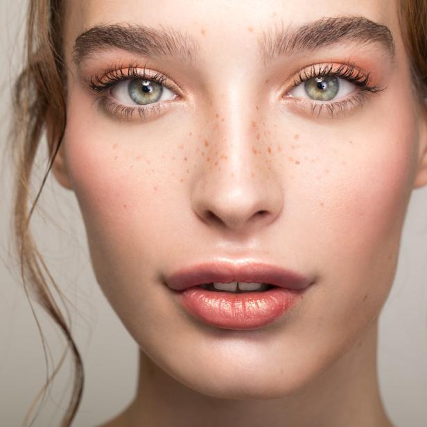 Porträt einer jungen Frau mit Sommersprossen und glänzendem Lippenstift.