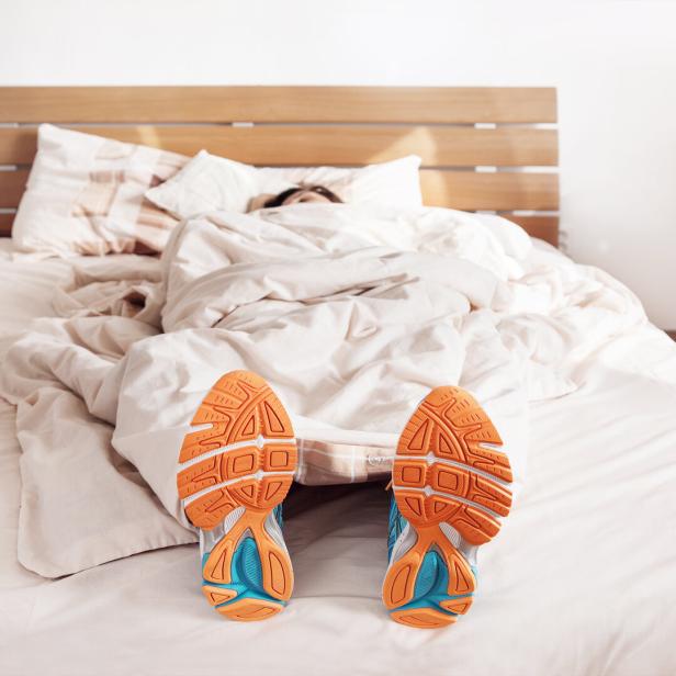 Eine Frau liegt mit Trainingsschuhen im Bett.