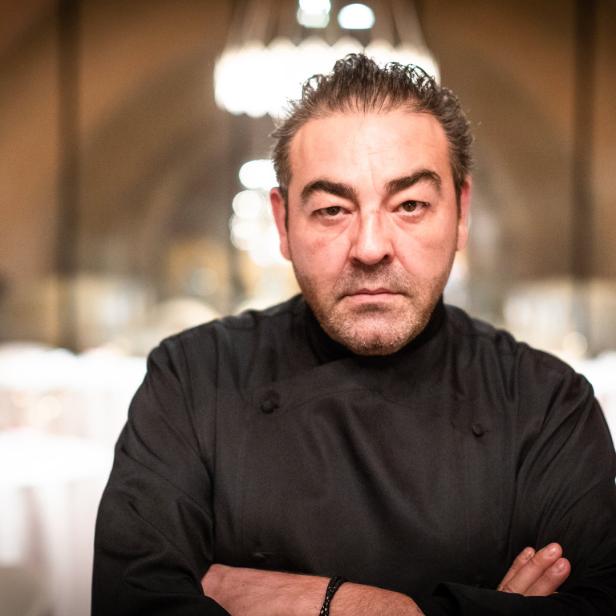 Ein Mann in Kochkleidung steht mit verschränkten Armen in einem Restaurant.