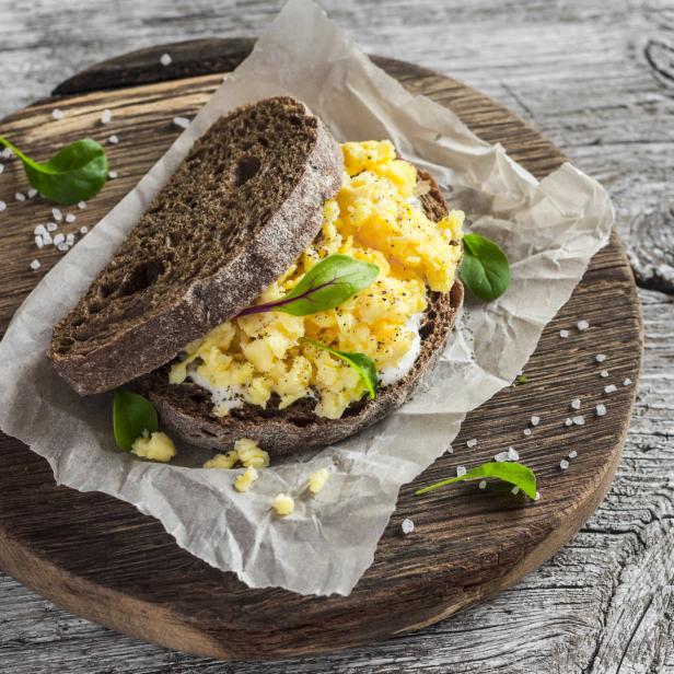 Ein Sandwich mit Rührei und Salat auf einem Holzbrett.