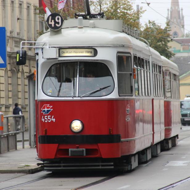 Eine rote und weiße Straßenbahn fährt auf dem Dr.-Karl-Renner-Ring in Wien.