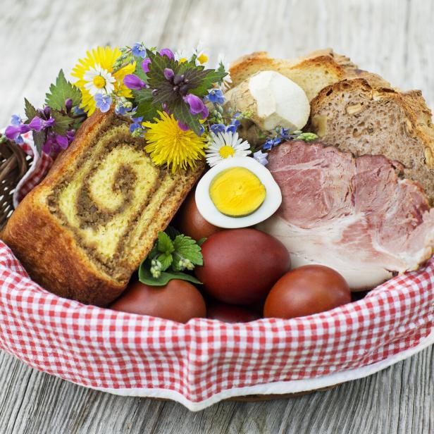 Eine Osterjause mit gefärbten Eiern, Schinken, Brot und Osterbrot in einem Korb.