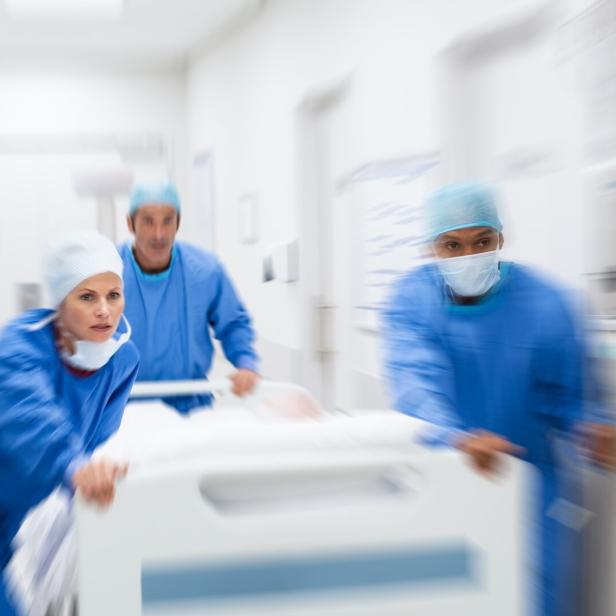 Drei medizinische Fachkräfte schieben ein Krankenhausbett durch einen Krankenhausflur.