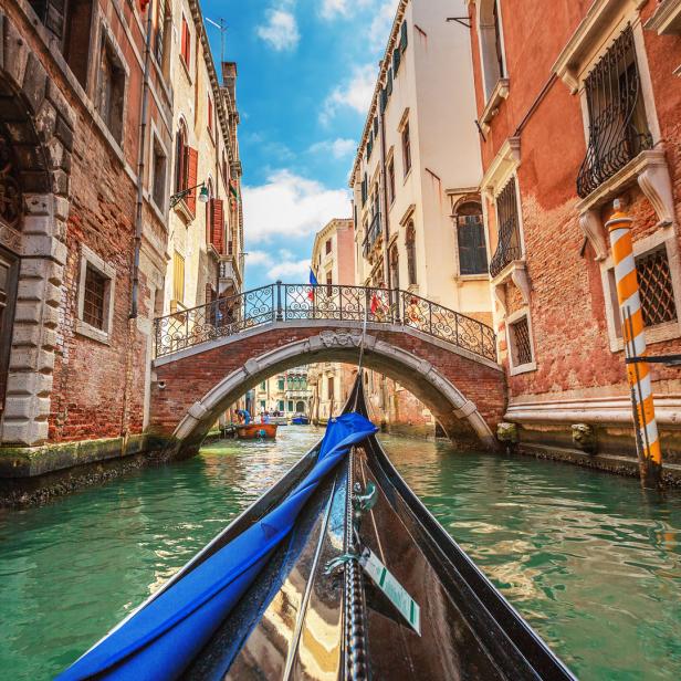 Eine Gondel fährt auf einem Kanal unter einer Brücke in Venedig hindurch.