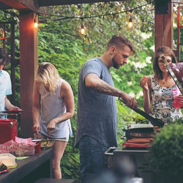 Eine Gruppe von Freunden grillt gemeinsam in einem Garten.