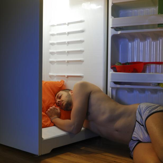 Ein Mann schläft mit einem orangefarbenen Kissen im Kühlschrank.