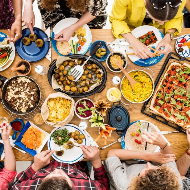 Eine Gruppe von Menschen isst gemeinsam an einem Tisch mit verschiedenen Speisen wie Pizza, Salat und Gemüse.