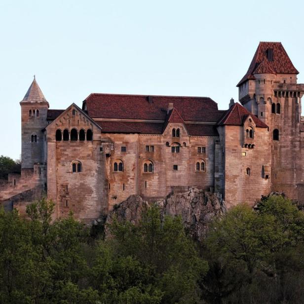 Burg Kreuzenstein thront auf einem Felsen über bewaldeten Hügeln.
