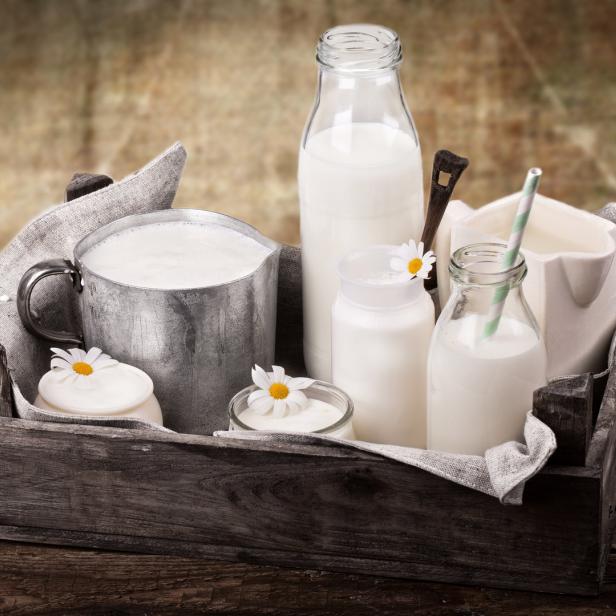 Verschiedene Milchprodukte in Gläsern und Krügen auf einem Holztablett.