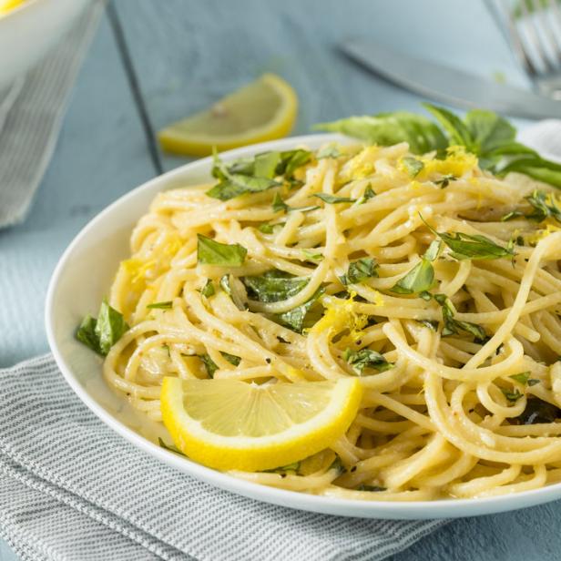 Ein Teller Spaghetti mit Zitrone und Basilikum auf einem Tisch.