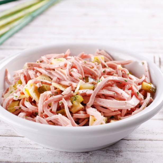 Ein Schüssel mit Wurstsalat, garniert mit Gurken und Kräutern.