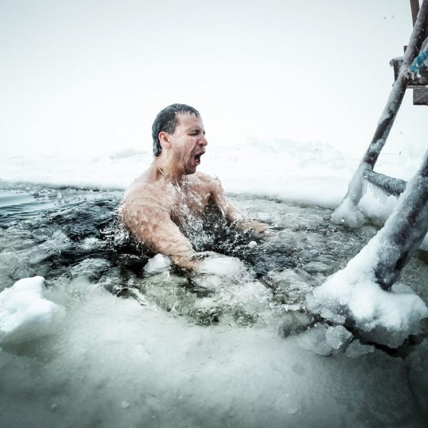 Ein Mann steigt in eiskaltes Wasser neben einer schneebedeckten Leiter.