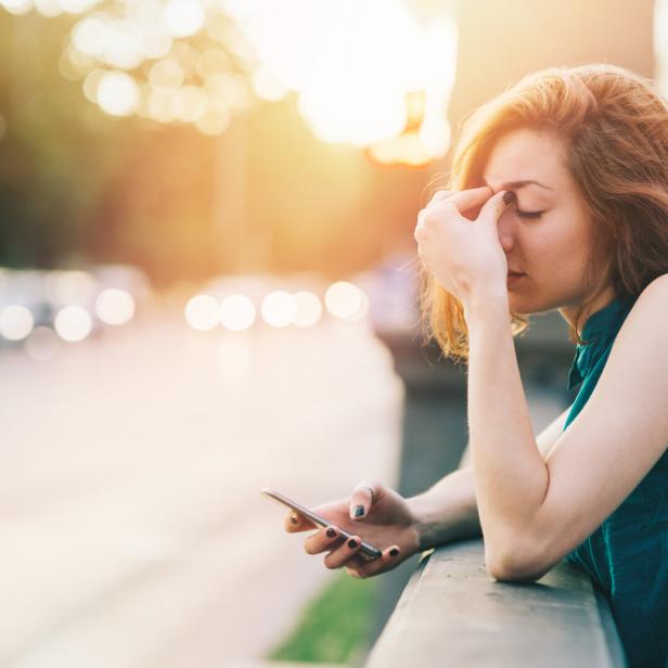Eine Frau mit einem Smartphone in der Hand wirkt gestresst.