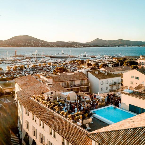 Blick auf Saint-Tropez mit Yachten, einem Pool auf einem Dach und einer Möwe im Flug.