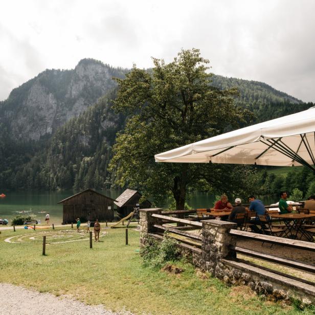 Menschen sitzen unter einem Sonnenschirm in einem Restaurant am Ufer eines Sees.