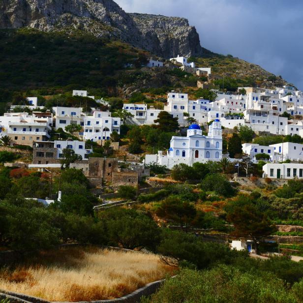 Ein griechisches Dorf mit weiß getünchten Häusern schmiegt sich an einen Hügel.