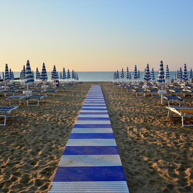 Ein Strand mit blau-weiß gestreiften Sonnenschirmen und Liegestühlen bei Sonnenaufgang.