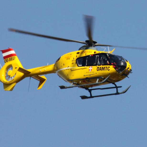 Ein gelber Rettungshubschrauber des ÖAMTC fliegt vor blauem Himmel.