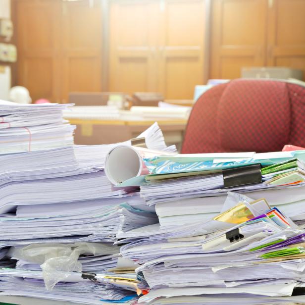 Ein Schreibtisch ist mit Papierstapeln und Büroartikeln überladen.