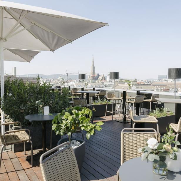 Eine Dachterrasse mit Tischen, Stühlen, Pflanzen und Blick auf Wien.