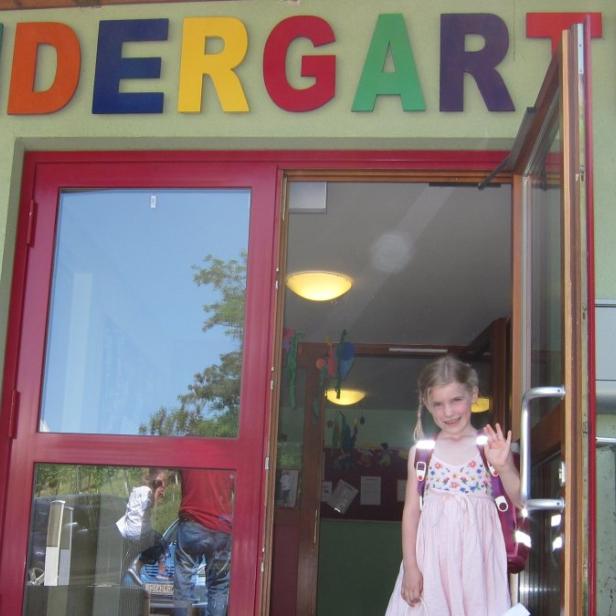 Ein Mädchen winkt vor dem Eingang eines Kindergartens.