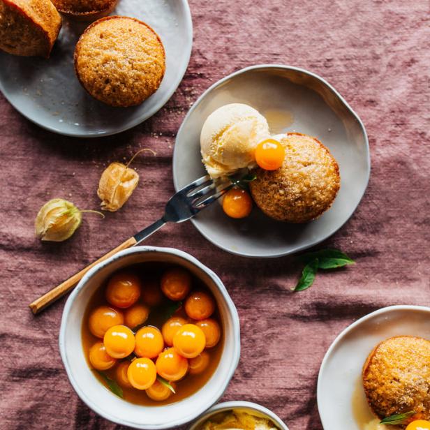Mehrere Teller mit Muffins, Eis und Physalis auf einer rosafarbenen Tischdecke.