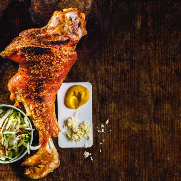 Ein Schweinshaxe mit Beilagen wie Krautsalat und Senf auf einem Holztisch.