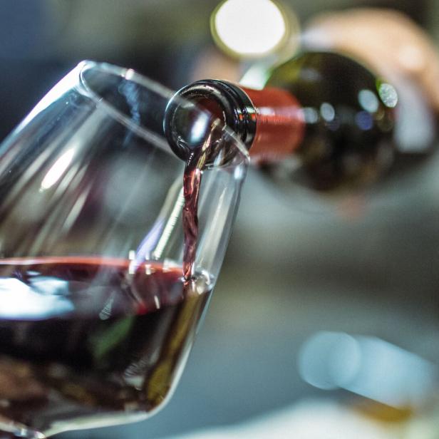 Rotwein wird aus einer Flasche in ein schräg gehaltenes Weinglas gegossen.