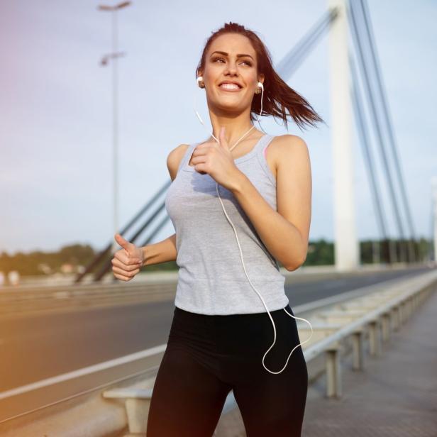 Eine junge Frau joggt mit Kopfhörern auf einer Brücke.