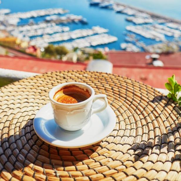 Eine Tasse Espresso auf einem Tisch mit Blick auf den Hafen von Neapel und den Vesuv.