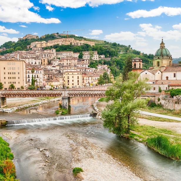 Blick auf eine italienische Stadt mit einem Fluss und einer Kirche mit grüner Kuppel.