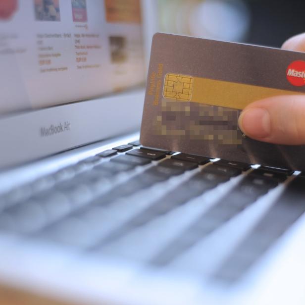 Eine Kreditkarte wird vor einem aufgeklappten Laptop gehalten.