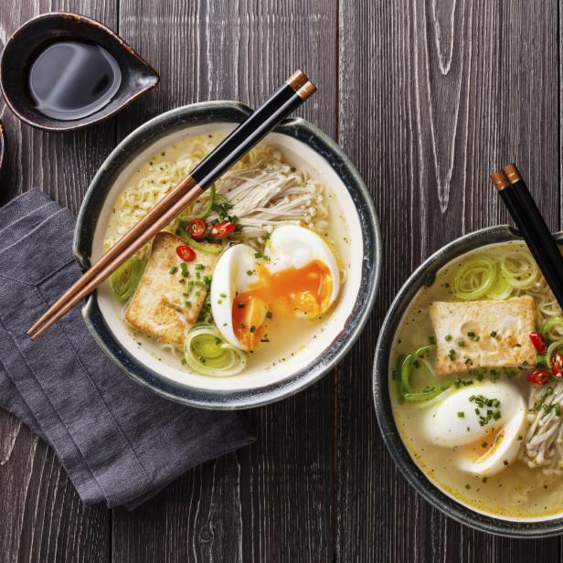 Zwei Schalen Ramen mit Tofu, Ei und Gemüse auf einem Holztisch.