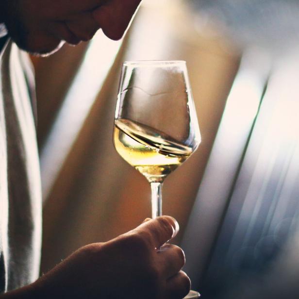 Junger Mann bei einer Weinverkostung mit einem Glas Wein in der Hand.