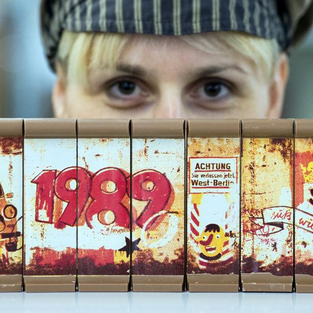 Eine Frau schaut über eine Miniatur-Berliner Mauer mit Graffiti und dem Datum 1989.