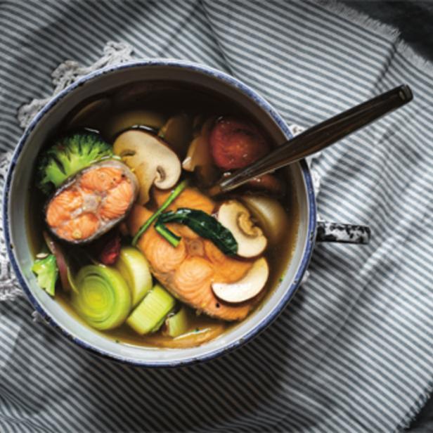 Eine Schüssel Fischsuppe mit Lachs, Gemüse und Pilzen auf einem gestreiften Tuch.