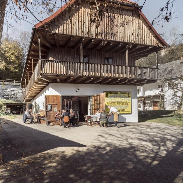 Gäste sitzen vor einem Gasthof mit dem Schriftzug „Unternberg Fernruf“.