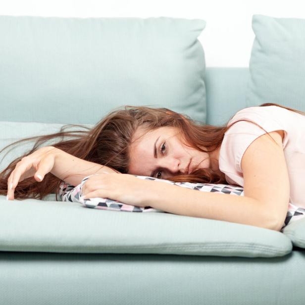 Eine junge Frau liegt erschöpft auf einem hellblauen Sofa.
