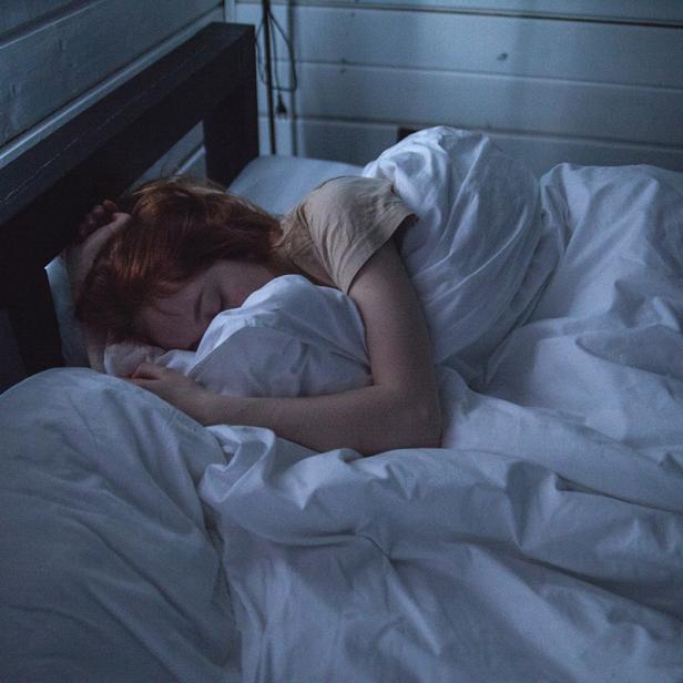 Eine Frau mit roten Haaren schläft in einem Bett mit weißer Bettwäsche.