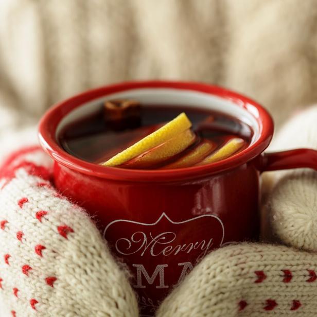 Hände in Fäustlingen halten eine volle Tasse Glühwein.