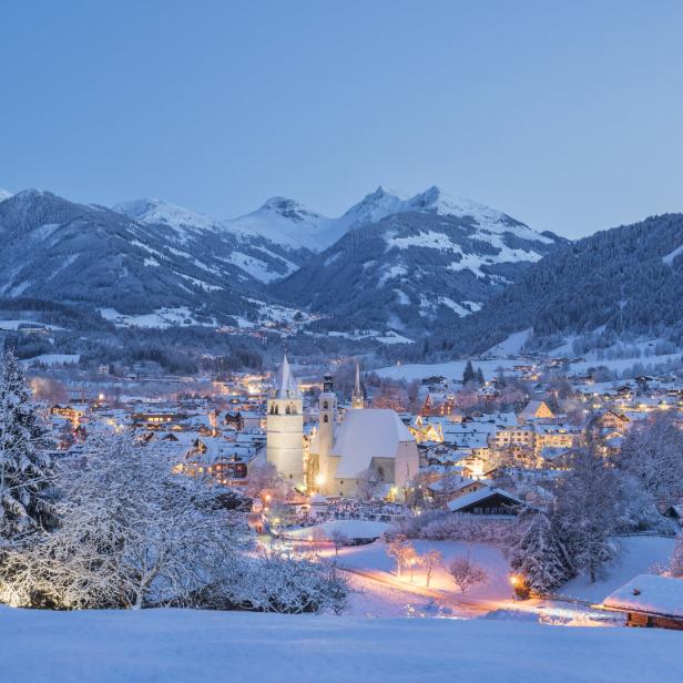 Ein verschneites Dorf liegt eingebettet in einer Berglandschaft bei Dämmerung.
