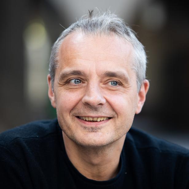 Ein lächelnder Mann mit grauen Haaren und blauen Augen blickt in die Kamera.
