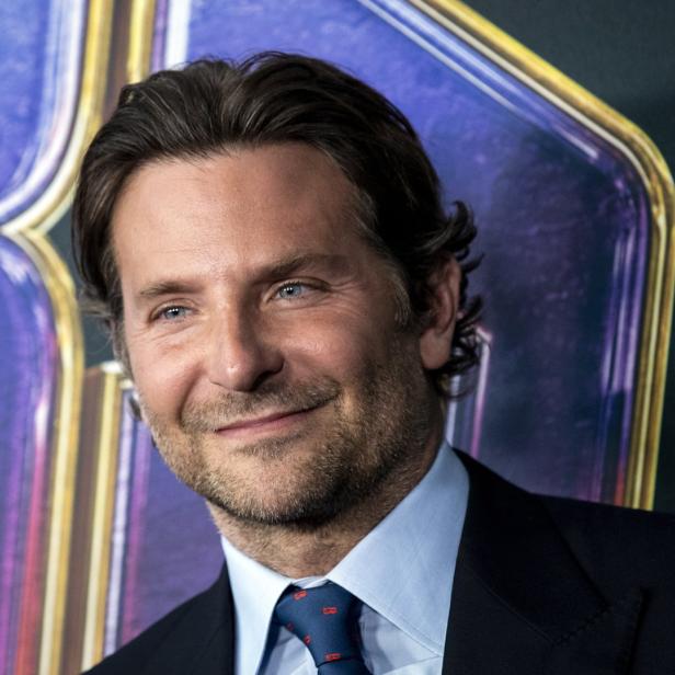 Porträt von Bradley Cooper mit Anzug und Krawatte vor einem farbigen Hintergrund.