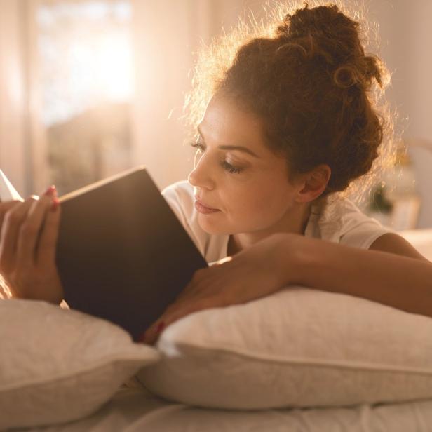 Eine Frau liegt im Bett und liest ein Buch.