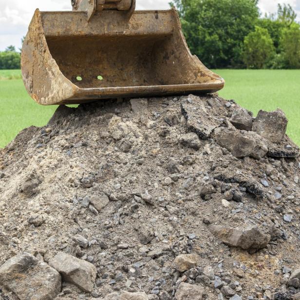 Eine Baggerschaufel ruht auf einem Haufen Erde und Steinen.