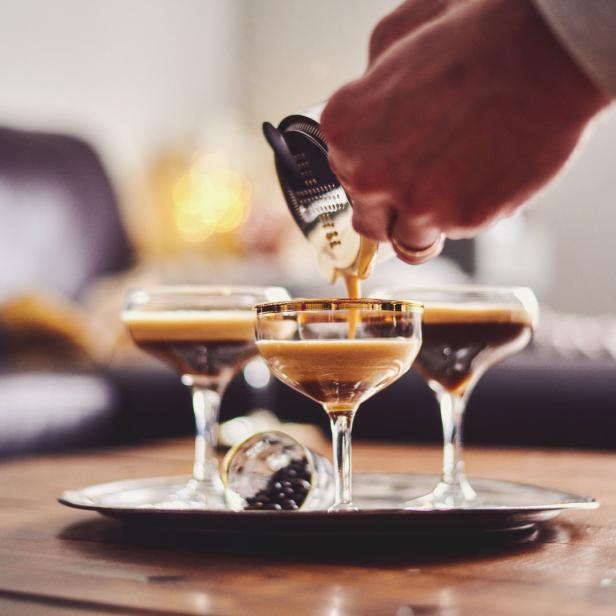 Eine Person gießt einen Espresso Martini in ein Glas mit Goldrand.